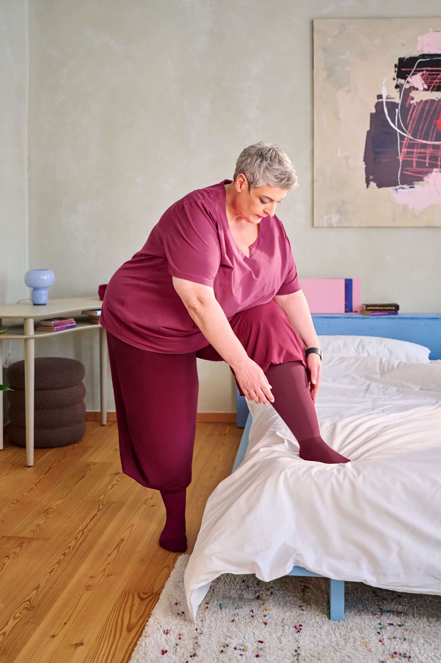 Frau sitzt auf einem Bett und zieht eine Kompressionsversorgung am Bein an